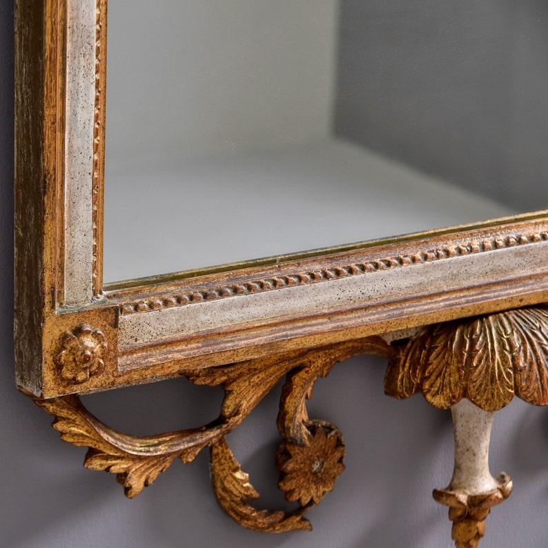 May include: A gold-toned ornate mirror with a decorative, scrolled, and carved frame. The mirror has a white and gold painted finish.