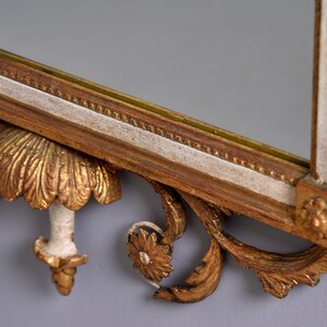 May include: A gold and white ornate mirror with a decorative carved frame. The frame features intricate floral and scrollwork designs.