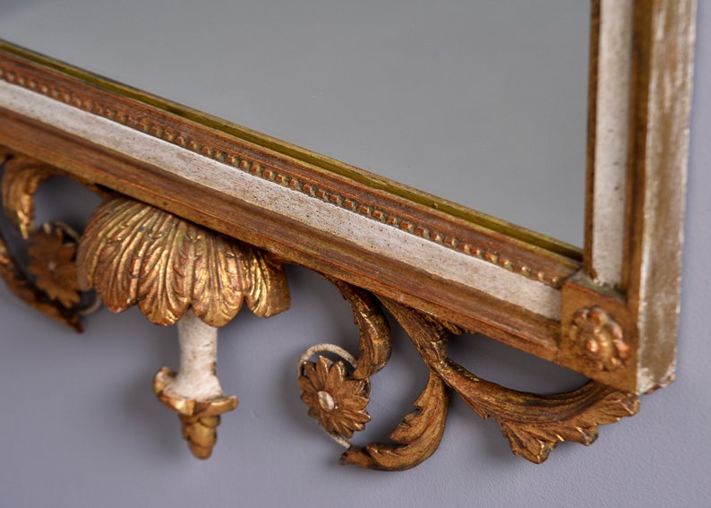 May include: A gold and white ornate mirror with a decorative carved frame. The frame features intricate floral and scrollwork designs.