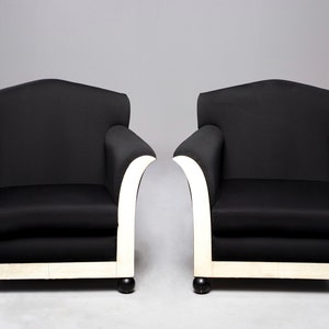 May include: Two black armchairs with white painted legs and a curved back. The chairs are upholstered in a black fabric and have a simple, elegant design.