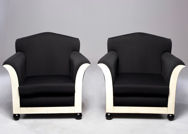 May include: Two black armchairs with white painted legs and a curved back. The chairs are upholstered in a black fabric and have a simple, elegant design.