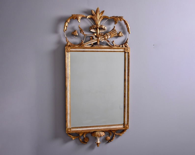 May include: A gold and white ornate mirror with a decorative top and a rectangular frame. The mirror has a beveled edge and a clear reflection.