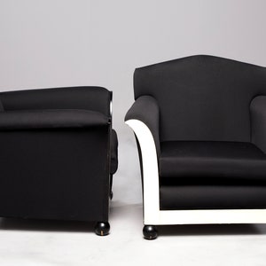 May include: Two black armchairs with white trim. The armchair on the left has black legs, while the armchair on the right has white legs.