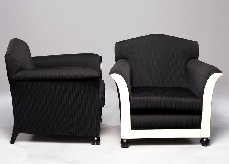 May include: Two black armchairs with white trim. The armchair on the left has black legs, while the armchair on the right has white legs.