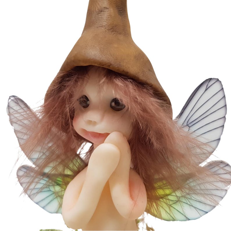 May include: A small fairy figurine with brown hair, a brown pointed hat, and iridescent wings. The fairy is holding its hands together in front of its chest.