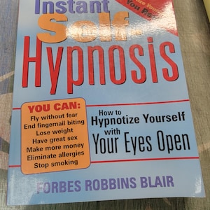 Peut inclure: Un livre intitulé "Instant Self Hypnosis" avec une couverture bleue et du texte rouge et orange. Le livre promet d'aider les lecteurs avec des problèmes tels que la peur, la perte de poids et le tabagisme. L'auteur est Forbes Robbins Blair.