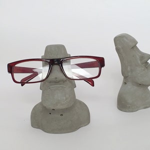 K&ouml;nnte beinhalten: Eine graue Betonskulptur eines Gesichts mit einer Brille darauf. Die Skulptur ist eine einzigartige und stilvolle M&ouml;glichkeit, Brillen zu halten.
