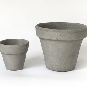 May include: Two gray ceramic flower pots, one larger than the other, on a white background.