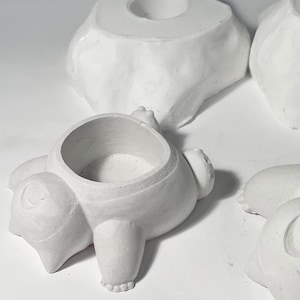 May include: Three white ceramic planters, one shaped like a rock, one shaped like a bear, and one shaped like a pig. Each planter has a small hole in the top for planting.
