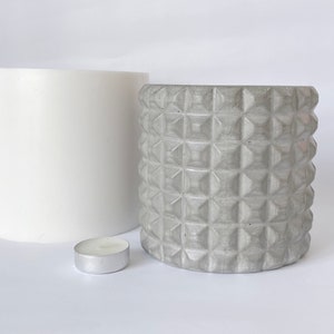 May include: Two concrete candle holders, one with a smooth surface and the other with a textured diamond pattern. A small silver candle sits in front of the holders.