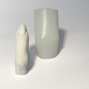 May include: A white plaster cast of a finger, next to a white silicone mold.