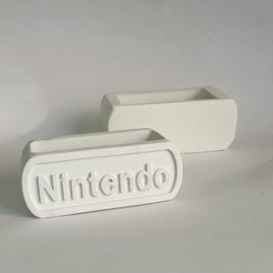May include: Two white ceramic planters, one with the word "Nintendo" embossed on the front.