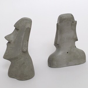 K&ouml;nnte beinhalten: Zwei graue Betonstatuen der Osterinselk&ouml;pfe. Die Statuen sind etwa 15 cm hoch und aus rauh strukturiertem Beton gefertigt.
