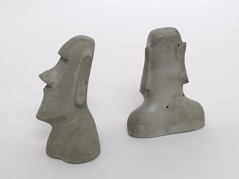 K&ouml;nnte beinhalten: Zwei graue Betonstatuen der Osterinselk&ouml;pfe. Die Statuen sind etwa 15 cm hoch und aus rauh strukturiertem Beton gefertigt.