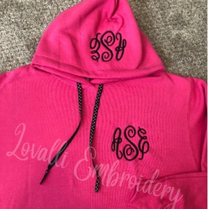 May include: A pink hooded sweatshirt with black embroidered initials "ASE" on the front and hood. The sweatshirt has a black drawstring with white polka dots.