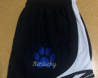 May include: Black running shorts with a white stripe down the side. The shorts have a blue paw print and the word "Kentucky" embroidered on the front.