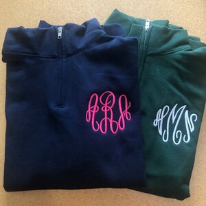 May include: A navy blue quarter-zip pullover with a hot pink embroidered monogram and a dark green quarter-zip pullover with a white embroidered monogram. Both garments feature a high collar with a silver-toned metal zipper closure.