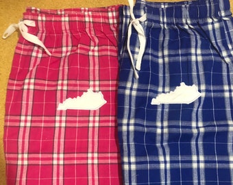 May include: Two pairs of plaid pajama pants. One pair is bright pink with white and red lines, the other is blue with white lines. Each pair has a white embroidered outline of the state of Kentucky.