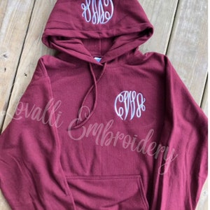 May include: Burgundy hooded sweatshirt with a white monogram embroidered on the front and hood. The monogram is the letters "CWS".