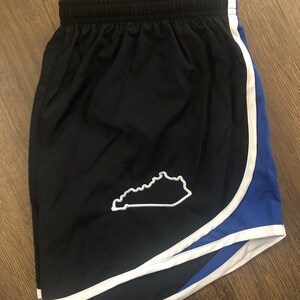May include: Black running shorts with a white outline and blue trim. The shorts have a white outline of the state of Kentucky on the left side.