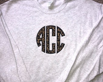 May include: A gray sweatshirt with a black and brown leopard print monogram of the letters "ACC" on the front.