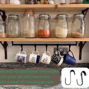 May include: Two light-coloured wooden shelves with black metal brackets. The top shelf holds glass jars with various grains. The bottom shelf features a black metal rail with five hanging mugs and two additional S-shaped hooks shown separately.