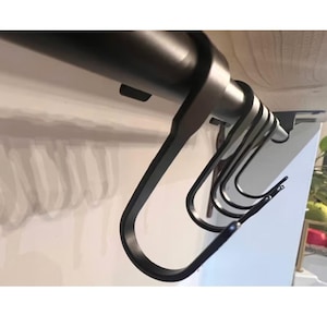 May include: A series of matte black metal S-hooks suspended from a horizontal black rod. Each hook features a curved, elongated design with a rounded bottom, providing a functional storage solution for hanging various items in a home or workspace.