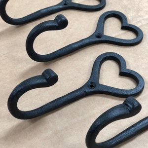 May include: Four black metal hooks with heart-shaped cut-outs. The hooks are designed for hanging items on a wall.