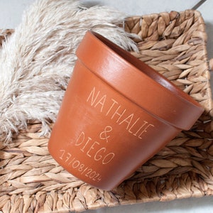 Peut inclure: Un pot de fleurs en terre cuite avec les noms "Nathalie & Diego" et la date "17/08/2024" gravés sur le côté.