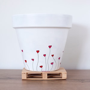 Peut inclure: Pot en terre cuite blanche avec des tiges noires peintes à la main et des cœurs rouges. Le pot est posé sur une petite palette en bois.