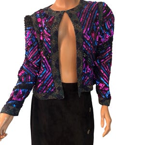 Puede incluir: Chaqueta vintage con lentejuelas en morado, azul y negro. La chaqueta tiene un dise&ntilde;o frontal abierto y hombros estructurados. Las lentejuelas est&aacute;n dispuestas en patrones geom&eacute;tricos, creando un efecto deslumbrante. Una pieza de moda vintage.