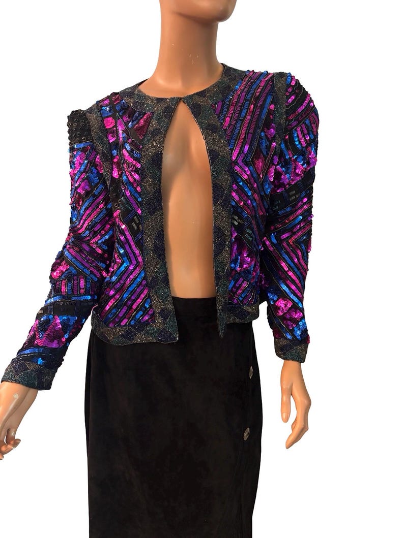 Puede incluir: Chaqueta vintage con lentejuelas en morado, azul y negro. La chaqueta tiene un dise&ntilde;o frontal abierto y hombros estructurados. Las lentejuelas est&aacute;n dispuestas en patrones geom&eacute;tricos, creando un efecto deslumbrante. Una pieza de moda vintage.