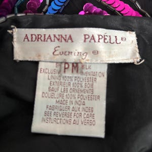 Puede incluir: Primer plano de una prenda de noche negra con lentejuelas y abalorios rosas y azules. La etiqueta dice "ADRIANNA PAPELL Evening". El forro es 100% poli&eacute;ster y el exterior es 100% seda.