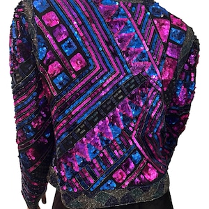 Puede incluir: Una chaqueta deslumbrante con un patr&oacute;n geom&eacute;trico de lentejuelas en tonos azules, morados y rosas. La chaqueta tiene mangas largas y una base negra, con un cuello y dobladillo brillantes. El dise&ntilde;o es intrincado y llamativo.