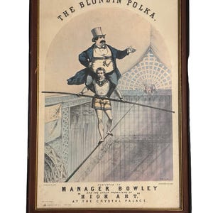 May include: Framed vintage poster titled "The Blondin Polka," featuring a tightrope walker carrying another person. The poster has a dark brown frame and includes text that reads "Dedicated to Manager Bowley and the other promoters of High Art at the Crystal Palace."