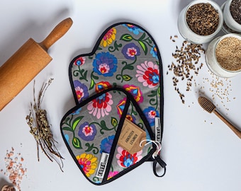 Puede incluir: Un juego de manopla y agarradera grises con un estampado floral en rojo, azul y amarillo. El juego está junto a un rodillo de madera, tarros de semillas y un cucharón de miel de madera. El juego tiene un ribete negro.