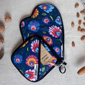 May include: A navy blue oven mitt and pot holder set with a floral pattern in pink, yellow, blue, and white. The set includes a tag with text. Walnuts, almonds, and a rolling pin are also present.