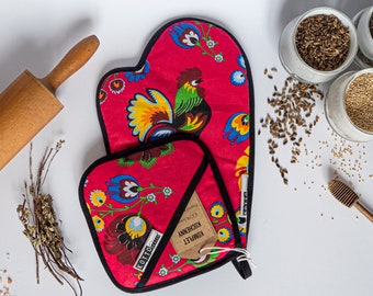 Puede incluir: Juego de manopla y agarradera rojos con diseño floral y gallo. También hay un rodillo de madera, tarros de semillas y un cucharón de miel en la imagen. La manopla y la agarradera tienen ribetes negros.