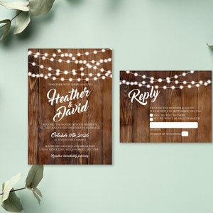May include: Wedding invitation and RSVP card set with a rustic wood background and string lights. The invitation features the names "Heather & David" in elegant script, along with event details. The RSVP card includes a reply section.