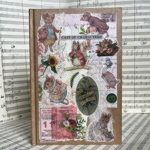 May include: A brown journal adorned with vintage animal illustrations and floral embellishments. The cover is a collage of stickers, including a squirrel, duck, and mouse. Text includes "CAST OF CHARACTERS" and "PAPERMAKER".