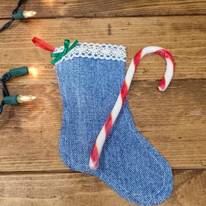Könnte beinhalten: Ein blauer Jeansstrumpf mit weißer Spitzenborte und einem roten und weißen Zuckerstangen. Der Strumpf ist mit einer grünen Schleife verziert und hängt an einer Holzoberfläche.