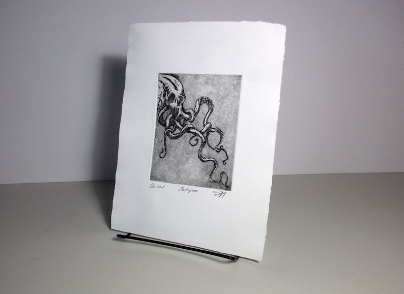 Puede incluir: Un grabado en blanco y negro de un pulpo. La obra de arte se presenta sobre papel blanco con un borde rugoso. El pulpo est&aacute; representado con tent&aacute;culos detallados y una cabeza en forma de calavera. La impresi&oacute;n se titula "Octopus" y est&aacute; firmada.