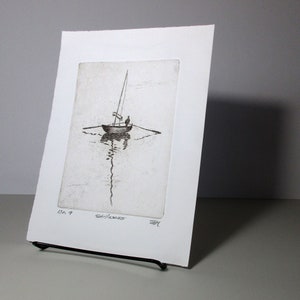 May include: A black and white etching of a sailboat on the water. The sailboat has a single sail and is being sailed by two people. The etching is framed in a white mat and has the number "7" and the word "Gillness" written on it.