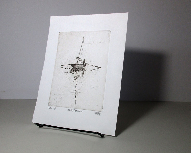 May include: A black and white etching of a sailboat on the water. The sailboat has a single sail and is being sailed by two people. The etching is framed in a white mat and has the number "7" and the word "Gillness" written on it.