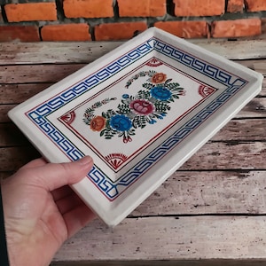 May include: White ceramic tray with a blue, red and yellow floral design. The tray has a decorative border with a blue and green pattern.