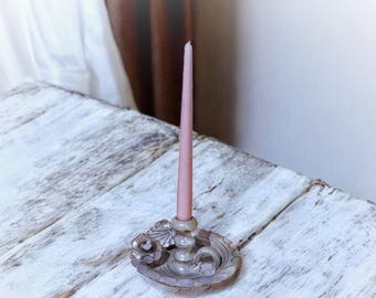 May include: A white ceramic candle holder with a floral design and a pink candle. The candle holder is on a white wooden surface.