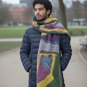 Puede incluir: Una bufanda de ganchillo hecha a mano con un patrón geométrico colorido. La bufanda presenta bloques de color púrpura, verde, amarillo, azul y gris. Se lleva sobre un abrigo azul marino, creando un accesorio cálido y elegante.