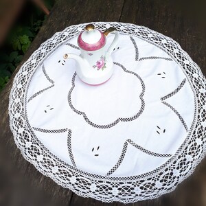 Può includere: Tovaglietta all'uncinetto in pizzo bianco con un motivo floreale e una teiera in porcellana bianca con accenti floreali rosa.