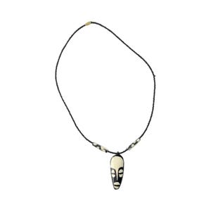 May include: A black beaded necklace with a white and black wooden mask pendant. The mask has a simple design with two eyes and a mouth.