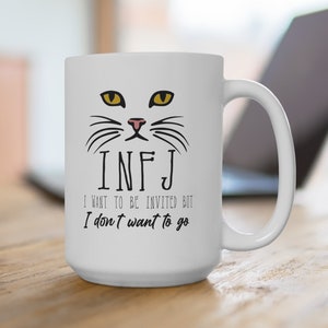 May include: White ceramic coffee mug with a black cat face and the text "INFJ I want to be invited but I don't want to go."